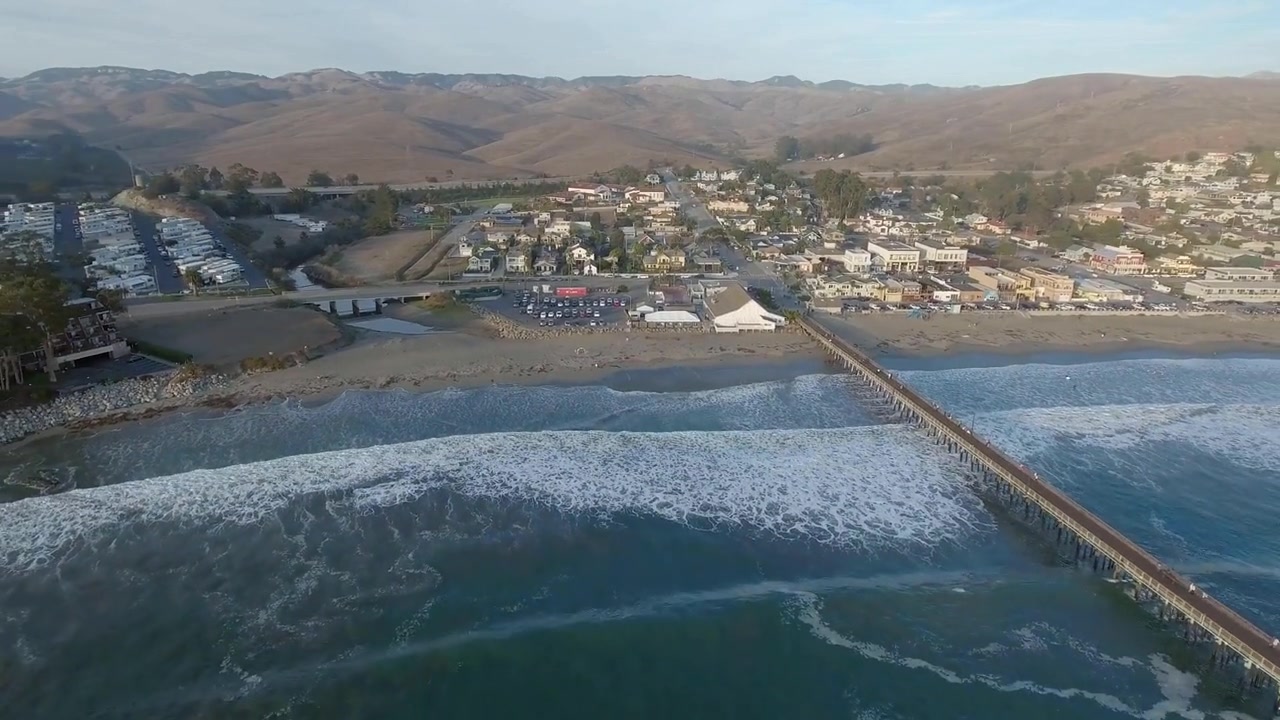 Cinematic sunset aerial over the Cayucos, California pier, shoreline, and coastal town