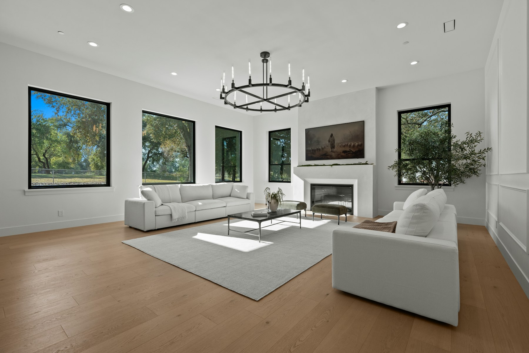 Spacious contemporary great room with fireplace, black-framed windows, and natural wood floors