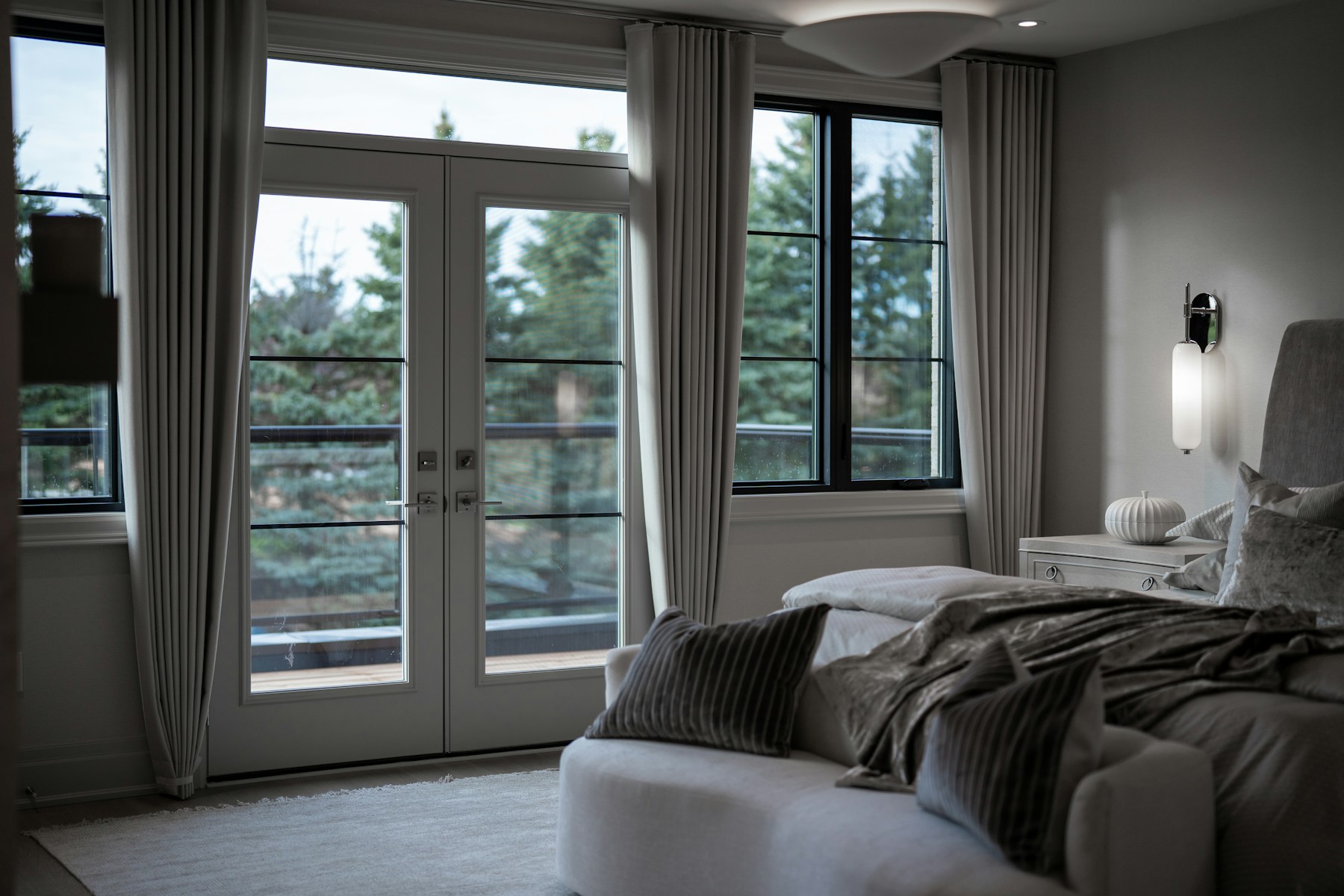 Luxury primary bedroom with tailored drapery, balcony doors, and layered neutral textiles